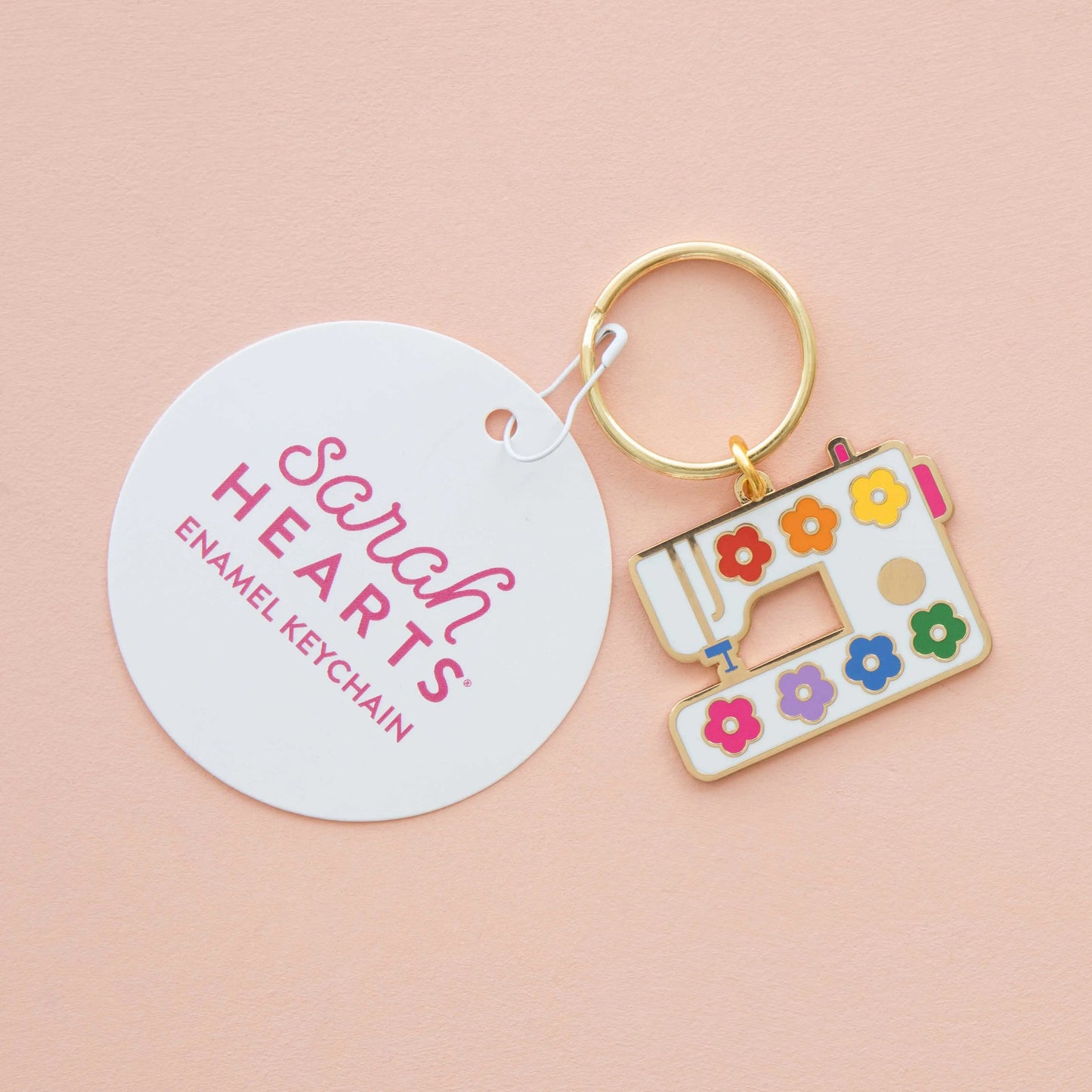 Enamel keychain shaped like a sewing machine with colorful flowers on a pink background