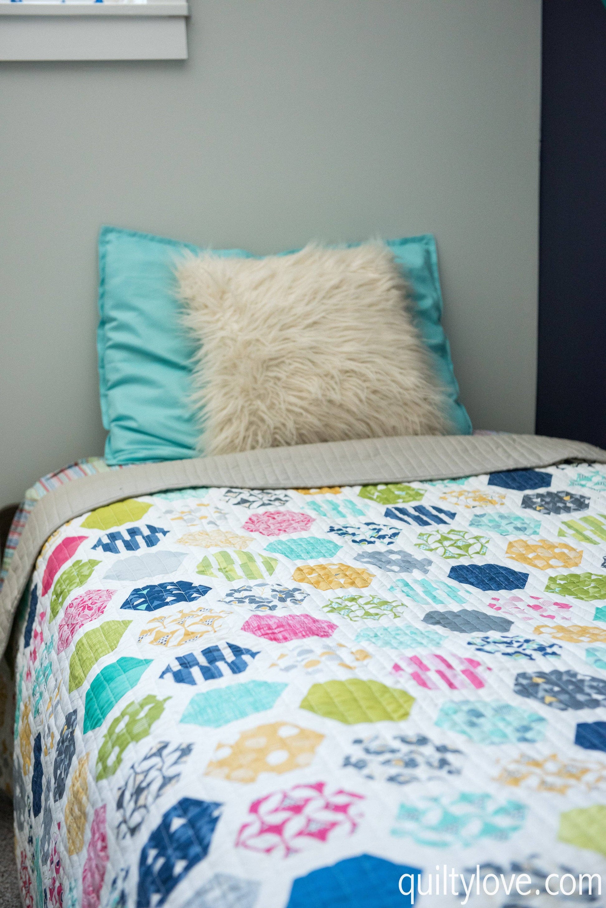 Colorful quilt with geometric pattern on a bed, featuring turquoise and beige pillows.