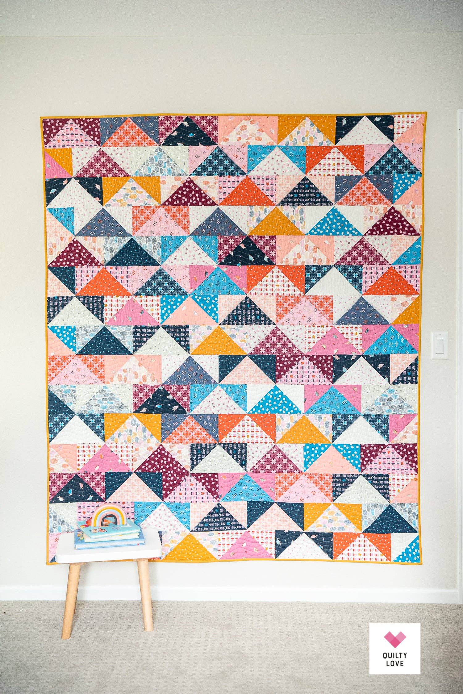 Colorful geometric quilt displayed on a stand against a white wall.