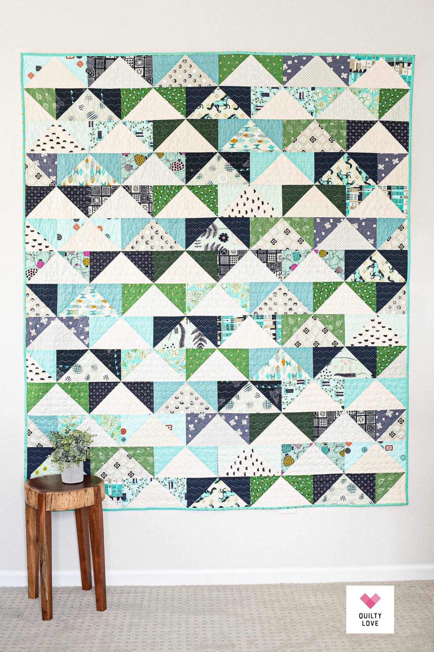Quilt with triangle pattern on a wall above a wooden side table.