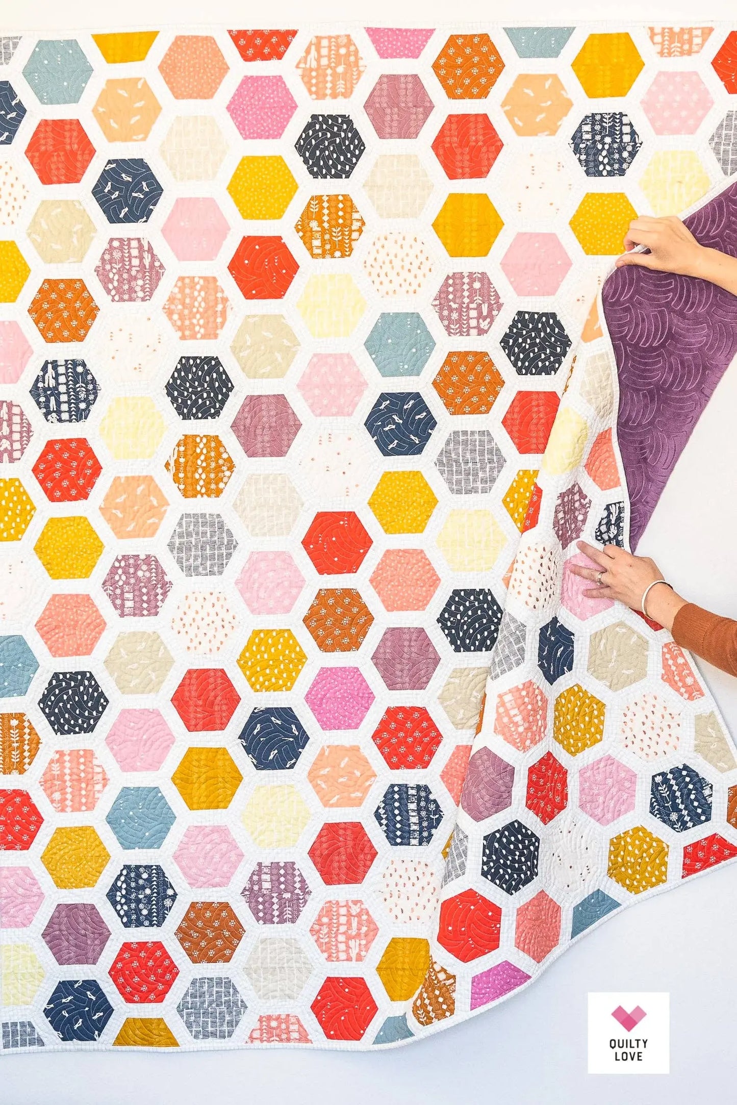 Hexagonal patterned fabric with a hand holding a piece of purple fabric.