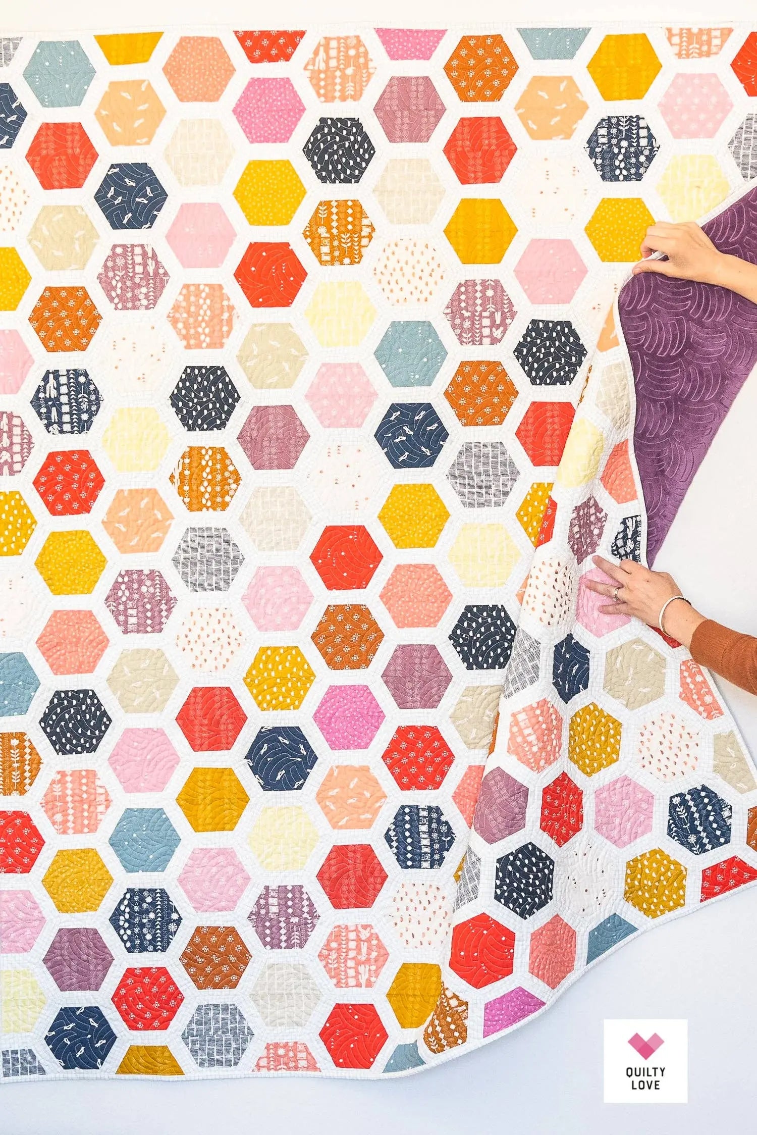 Hexagonal patterned fabric with a hand holding a piece of purple fabric.
