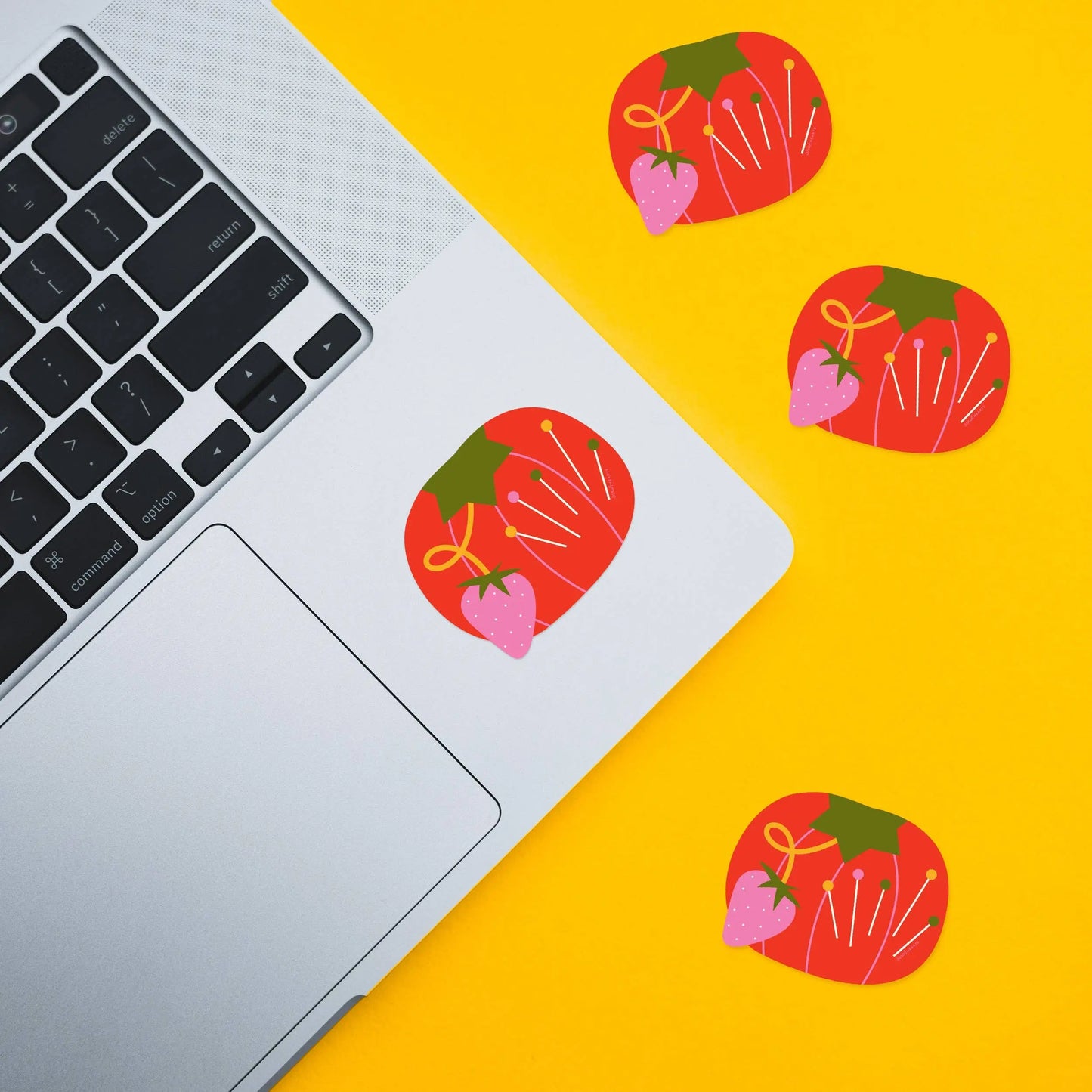Laptop on a yellow surface with decorative tomato pin cushion stickers.