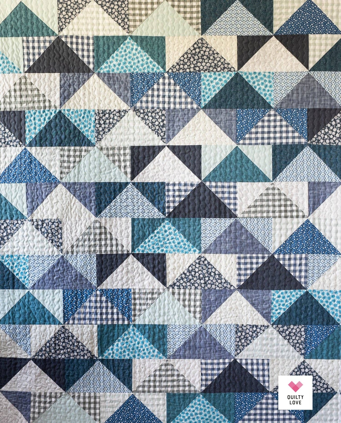 Quilt with geometric triangle pattern in various blue tones, featuring the brand 'Quilty Love'.