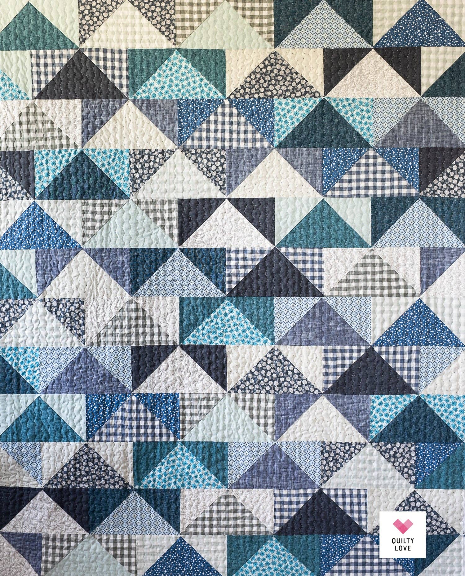 Quilt with geometric triangle pattern in various blue tones, featuring the brand 'Quilty Love'.