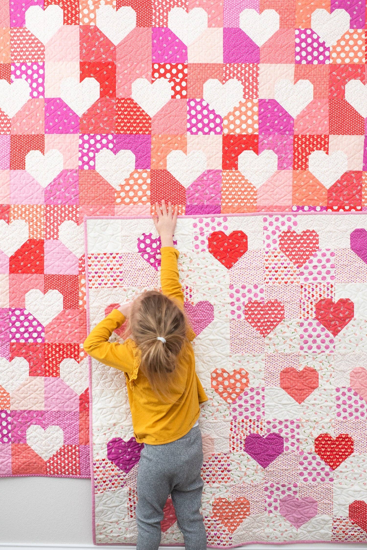 Child in a yellow shirt standing on a heart-patterned quilt with a colorful heart design.