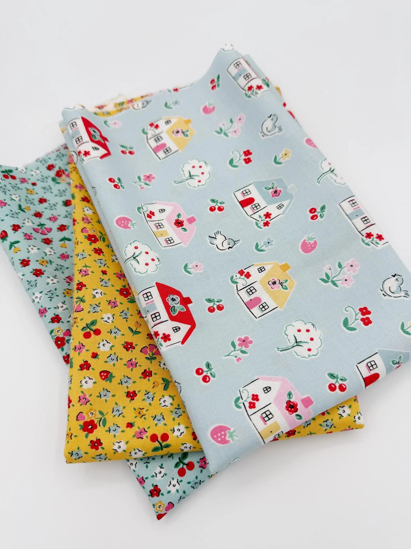 Three pieces of fabric with house and cherry patterns on a white background