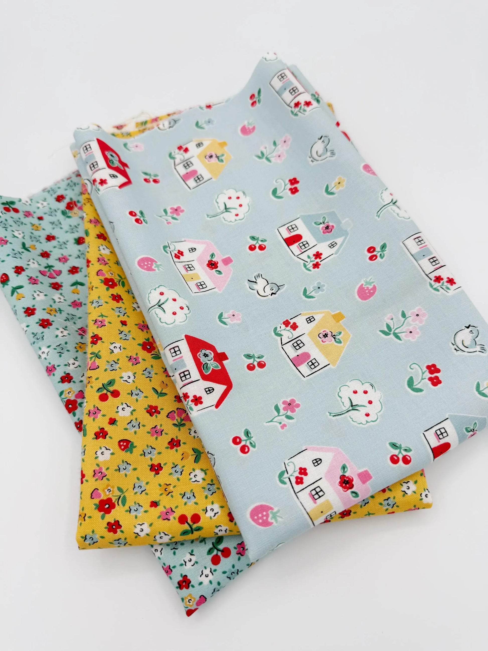 Three pieces of fabric with house and cherry patterns on a white background
