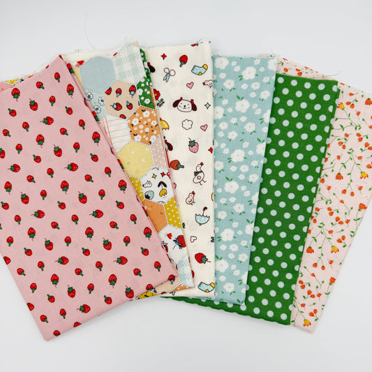 Fanned stack of coordinating quilting cotton fat quarters featuring pink strawberry print, patchwork hexagon print, cream fabric with dogs and strawberries, blue floral print, green polka dot, and pink floral vine print