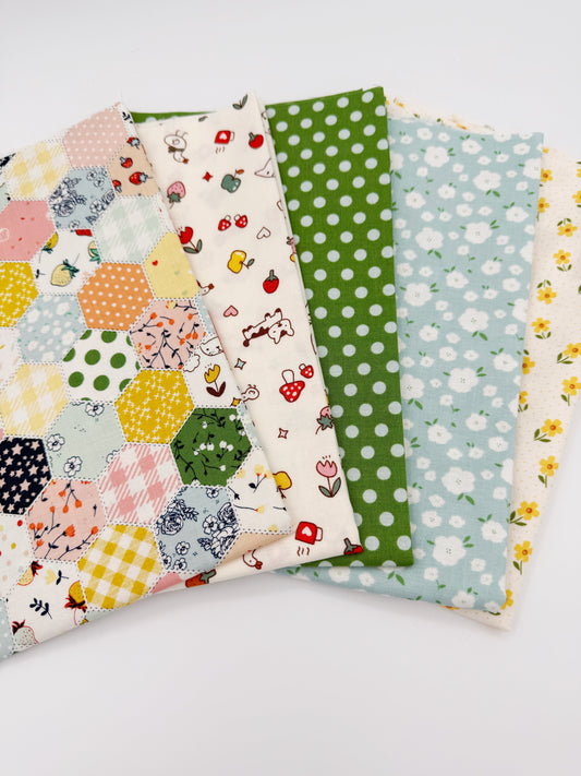 Fanned stack of coordinating quilting cotton fat quarters featuring multicolor patchwork hexagon print, cream fabric with strawberries and puppy, green polka dot, blue floral, and cream fabric with yellow flowers