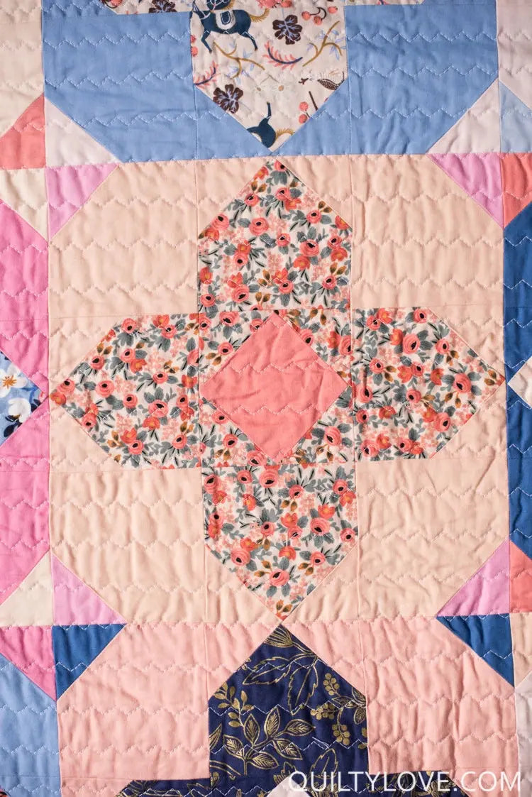 Quilt with floral patterns and geometric shapes on a pink background