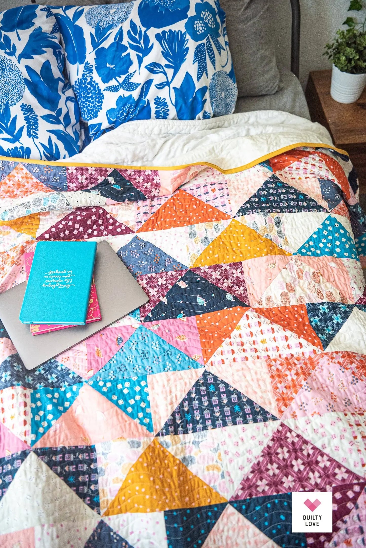 Colorful quilt with geometric patterns on a bed, featuring a notebook and pen.