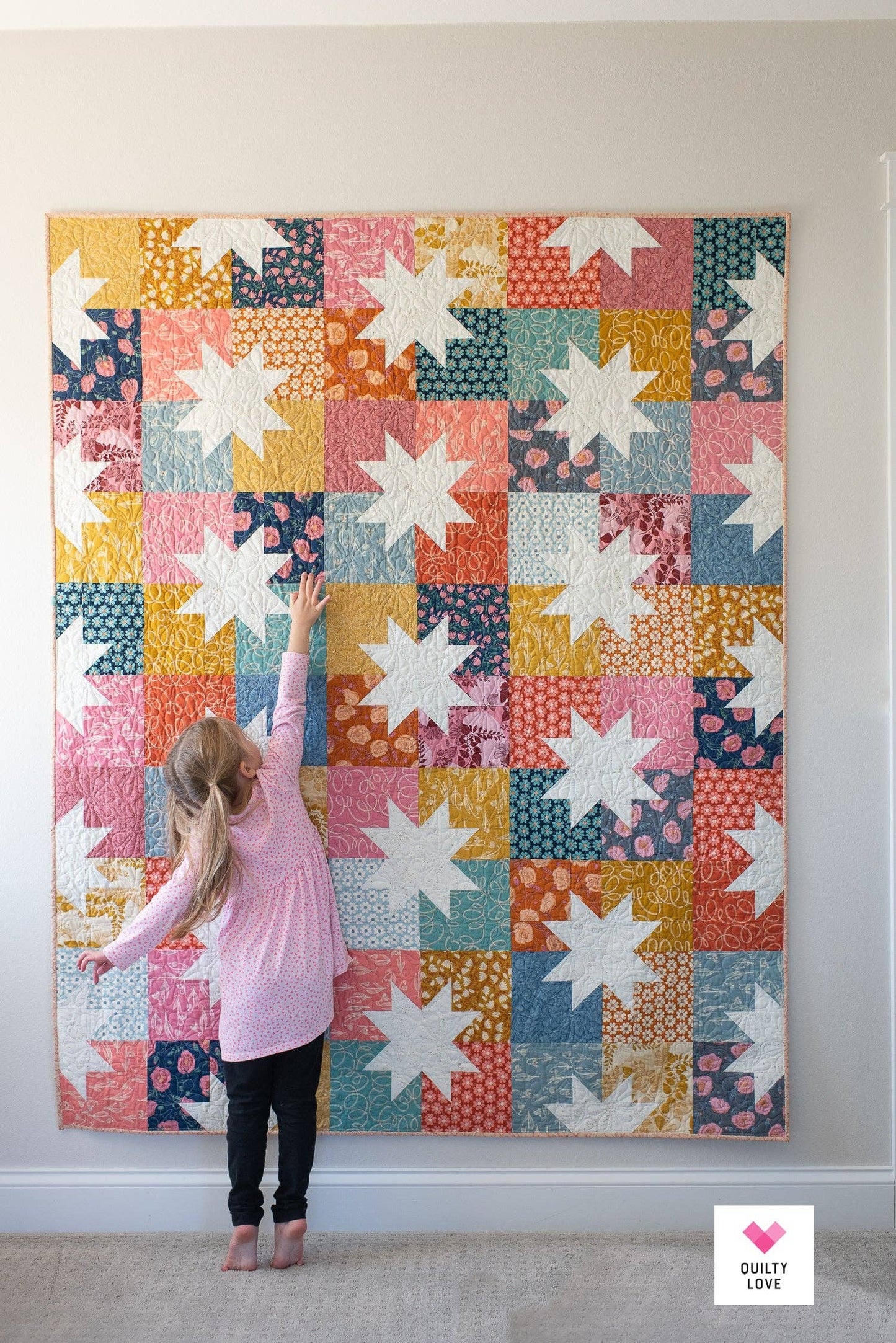Colorful star-patterned quilt on a wall with a person touching it